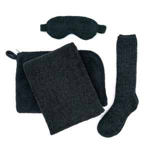 Soft black eye mask, cozy socks, plush blanket, and matching pouch arranged flat as part of the Travel Set (Blanket, Socks, Eyemask, Bag) | Kashwére for wellness and relaxation.