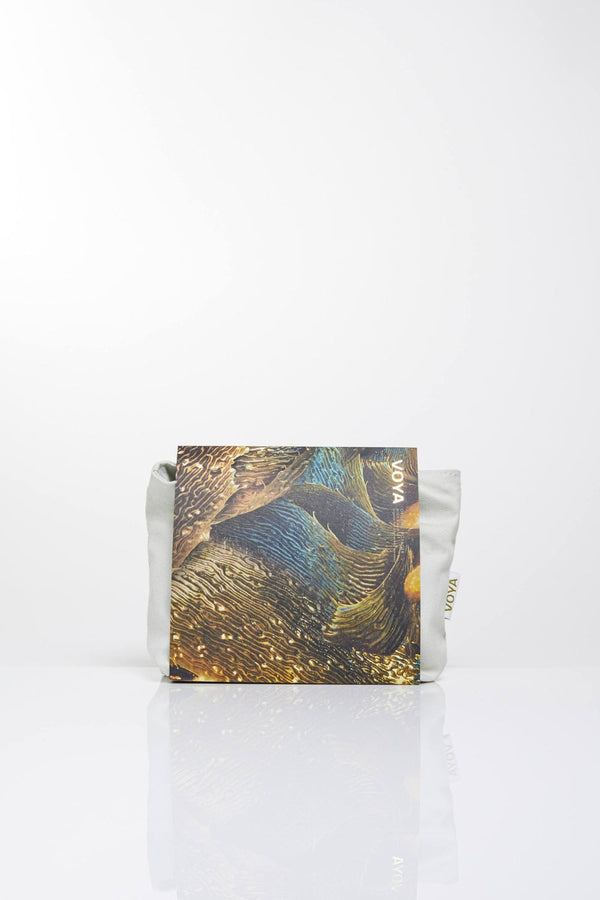 Organized Organic Voyager Travel Set | VOYA with artistic textured packaging resting against a light fabric pouch on a clean white background, promoting skincare and wellness.
