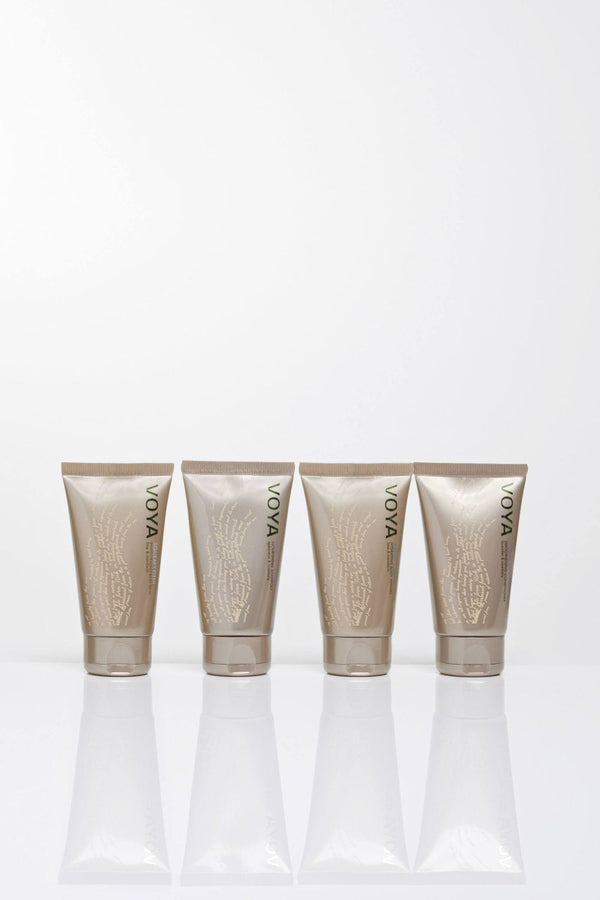 Four beige tubes of skincare products with green VOYA branding lined up, showcasing the Organic Voyager Travel Set | VOYA for body care and wellness.