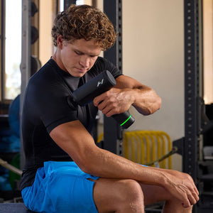 Man in gym wearing black shirt and blue shorts using Hypervolt 3 Pro | Hyperice percussion massage device on his arm muscle for recovery and wellness.