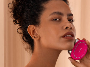 Woman using the bright pink BEAR™ 2 | FOREO facial toning device for skincare, highlighting wellness and body care routines.
