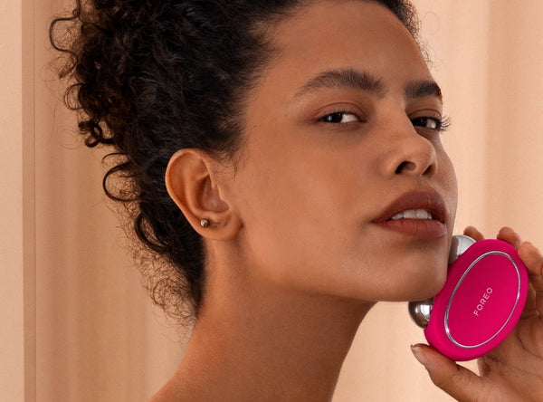 Woman using the bright pink BEAR™ 2 | FOREO facial toning device for skincare, highlighting wellness and body care routines.