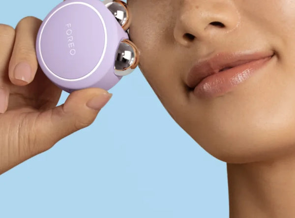 Close-up of a woman using the BEAR™ 2 Go | FOREO facial device on her cheek, demonstrating a compact skincare and wellness tool for radiant skin.