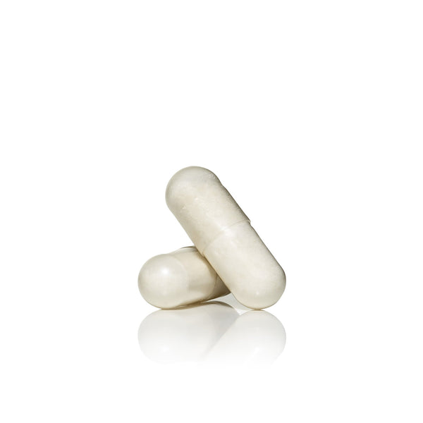 Two white capsules on a reflective surface representing skincare and wellness supplements from Skin Youth Biome™ | Jane Iredale.