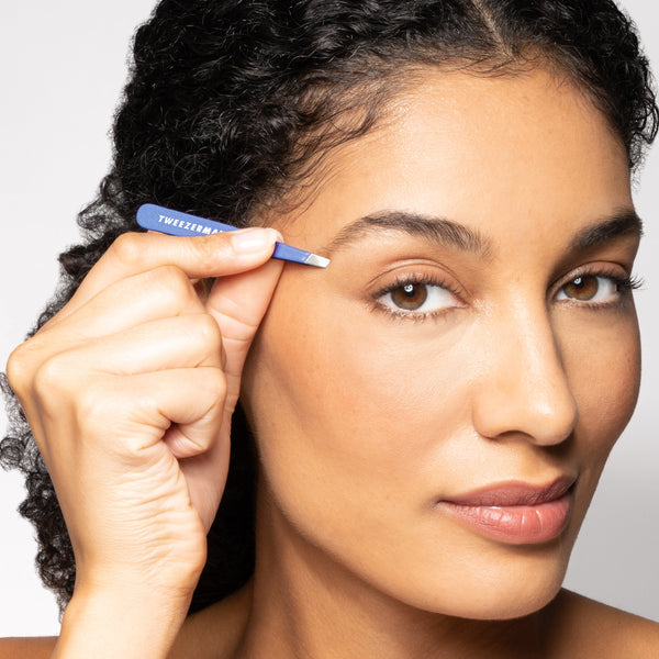 Woman using the Granite Sky Mini Slant Tweezer | Tweezerman to groom her eyebrow, showcasing precise skincare and beauty grooming tool.