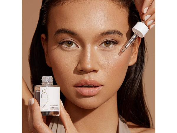 Close-up of a woman applying Hyaluronic Self Tanning Serum | NUDA to her face with a dropper, showcasing smooth, glowing skin and skincare body care routine.