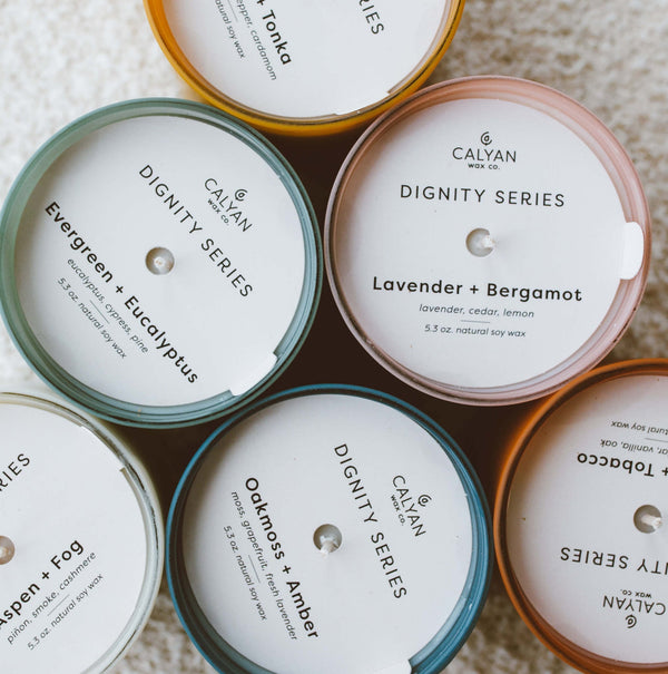 Vetiver + Tonka Dignity Series Glass Jar Soy Candle | Calyan Wax Co. - 5.3 oz displayed among other scented candles arranged in a circle on a soft surface.