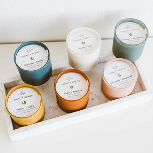 Vetiver + Tonka Dignity Series Glass Jar Soy Candle | Calyan Wax Co. - 5.3 oz displayed among five other scented candles in colorful glass jars on a white marble tray.