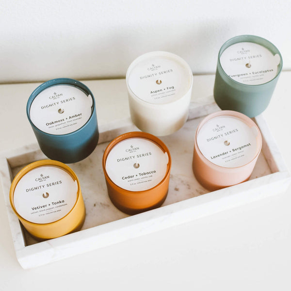 Vetiver + Tonka Dignity Series Glass Jar Soy Candle | Calyan Wax Co. - 5.3 oz displayed among five other scented candles in colorful glass jars on a white marble tray.