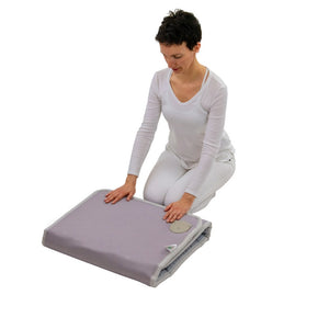 Woman in white clothing folding a light purple wellness mat labeled Platinum-Mat™ Full Short 6024 Firm - Photon Advanced PEMF InfraMat Pro® | HealthyLine used for body care and recovery tools.