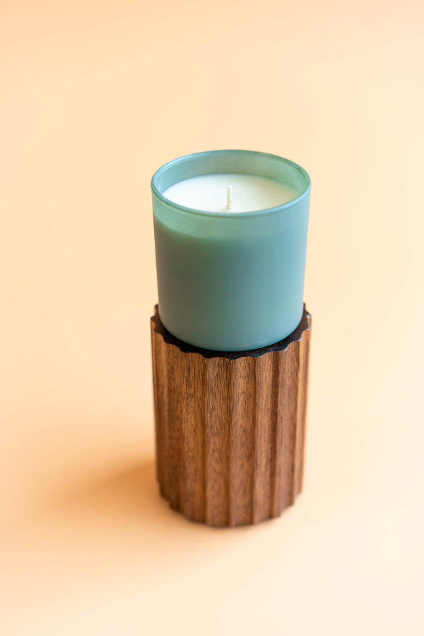 Evergreen + Eucalyptus Dignity Series Glass Jar Soy Candle | Calyan Wax Co. - 5.3 oz displayed in a light green frosted glass container on a wooden textured holder against a soft beige background.