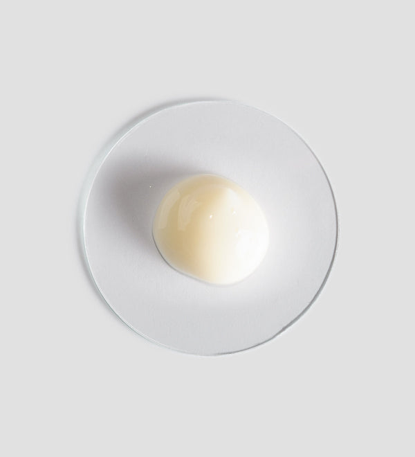 A smooth, creamy beige sample of Sublime Skin Corrector | [ comfort zone ] skincare product on a clear round surface, highlighting its texture and consistency.