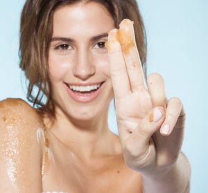 Woman smiling with exfoliating body polish on her fingers and shoulder, demonstrating Bourbon Bubbler Liquor Infused Body Polish | Farmhouse Fresh for skincare and body care.