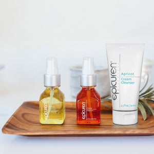 Clear glass bottle of Citrus Herbal Cleanser | Epicuren Discovery with yellow liquid alongside two other Epicuren Discovery skincare products on a wooden tray for skincare and wellness.