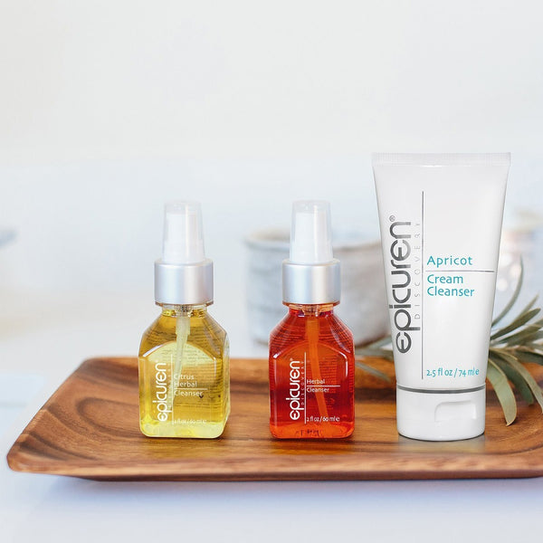 Clear glass bottle of Citrus Herbal Cleanser | Epicuren Discovery with yellow liquid alongside two other Epicuren Discovery skincare products on a wooden tray for skincare and wellness.