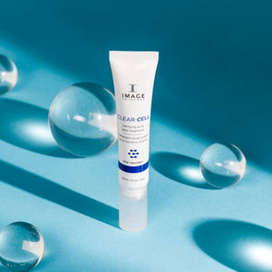 CLEAR CELL clarifying acne spot treatment | IMAGE Skincare tube standing on a blue surface with glass spheres and soft shadows, representing skincare and wellness supplements.