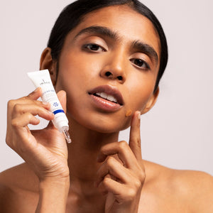 Woman applying CLEAR CELL clarifying acne spot treatment | IMAGE Skincare on her cheek, demonstrating skincare use for acne care and clear skin.