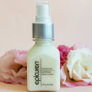 Colostrum Luminous Glow Cream | Epicuren Discovery skincare product in a white pump bottle with soft pink and white flowers in the background.