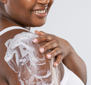 Woman applying Ahhhsome Relief™ Foam-to-Oil After Sun Body Mousse | Farmhouse Fresh on her shoulder with a smile, demonstrating soothing skincare and body care.