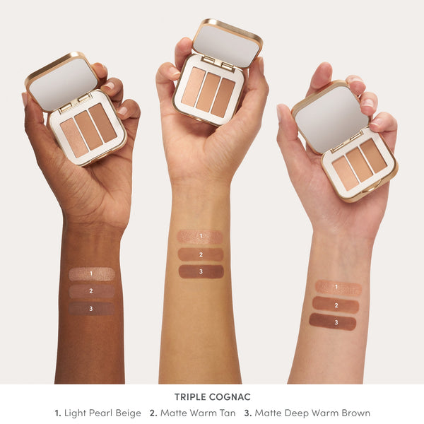 Three hands holding Purepressed Eye Shadow Triple | Jane Iredale in warm neutral shades with numbered swatches on arms showing Light Pearl Beige, Matte Warm Tan, and Matte Deep Warm Brown colors.