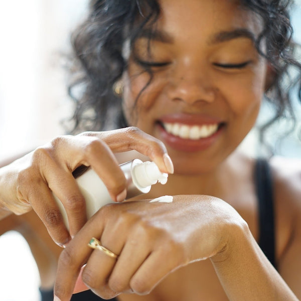 Woman smiling as she applies a white cream on her hand, demonstrating the use of Facial Emulsion Enzyme Moisturizer | Epicuren Discovery for skincare and hydration.