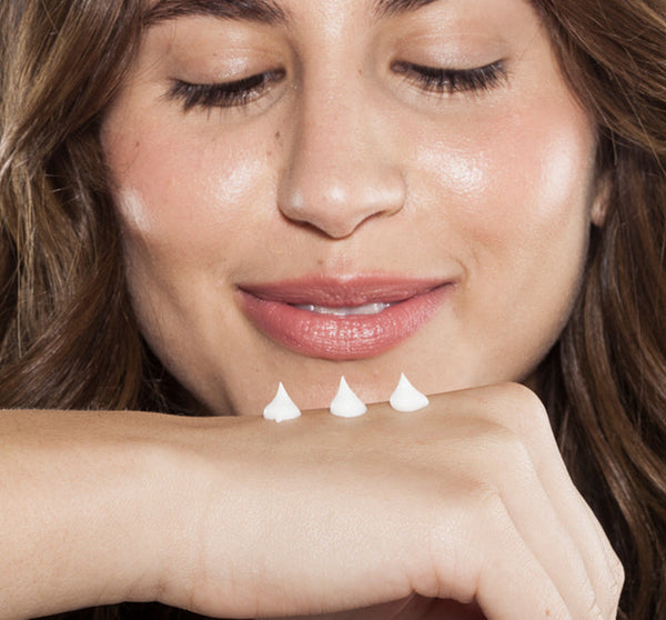 A woman smiling gently while applying three small dollops of Fluffy Bunny Shea Butter | Farmhouse Fresh on the back of her hand, showcasing smooth, hydrated skin.