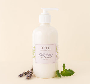 A white pump bottle of Fluffy Bunny Shea Butter | Farmhouse Fresh body lotion displayed with sprigs of lavender and fresh mint leaves on a neutral background.