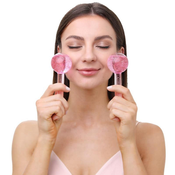 A woman gently pressing two pink Glow Globes [Ice Roller for Face] | Dreambox Beauty against her cheeks with a relaxed expression, promoting skincare and wellness.