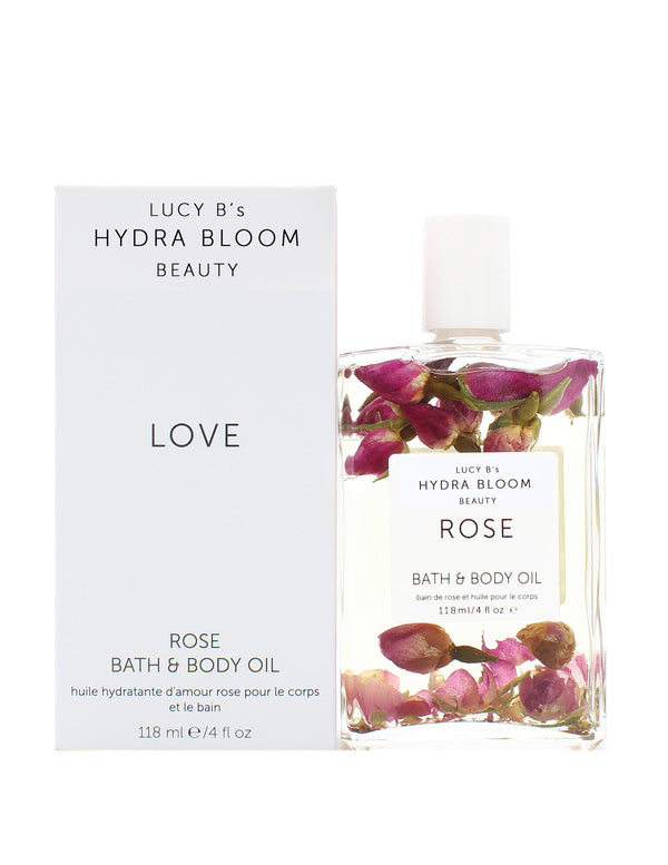Clear bottle of Rose Bath & Body Oil | Hydra Bloom with visible rose petals inside, next to its white packaging box labeled for skincare and body care use.