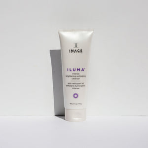 Tube of ILUMA intense brightening exfoliating cleanser | IMAGE Skincare standing upright on a white surface with minimal shadows, highlighting the sleek white packaging in a minimalistic setting.