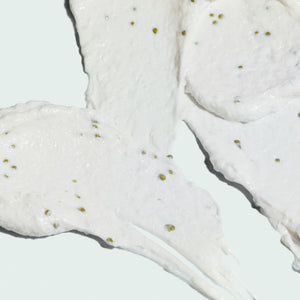 Close-up texture of a white exfoliating cleanser with small green exfoliating beads, highlighting the creamy consistency of ILUMA intense brightening exfoliating cleanser | IMAGE Skincare.