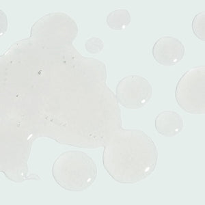 Clear liquid serum droplets and a small pool of gel-like skincare product on a light background, representing ILUMA intense facial illuminator | IMAGE Skincare.