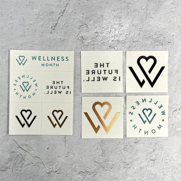 Set of temporary "Wellness Month Tattoos | Wellness Month" featuring motivational text and heart-themed logos in black, gold, and teal on white background.