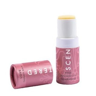 Opened stick of Love Therapy Balm | Scentered in pink packaging with white text, featuring scent details rose, patchouli, and cedarwood for skincare and wellness.