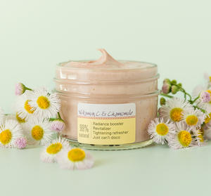 Jar of Mighty Brighty™ Vitamin C + Chamomile Brightening Mask | Farmhouse Fresh with light pink cream surrounded by fresh chamomile flowers on a pale green background representing natural skincare and radiance booster.