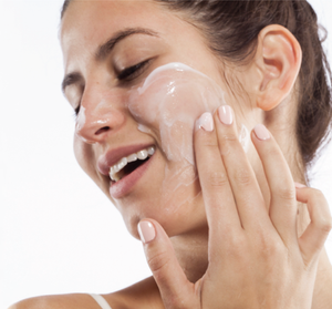 Woman gently applying Mighty Brighty™ Vitamin C + Chamomile Brightening Mask | Farmhouse Fresh to her cheek, showcasing smooth skincare routine and radiant skin.