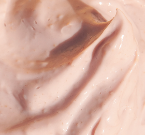 Close-up of smooth, creamy light peach skincare mask texture with small exfoliating particles, representing Mighty Brighty™ Vitamin C + Chamomile Brightening Mask | Farmhouse Fresh.