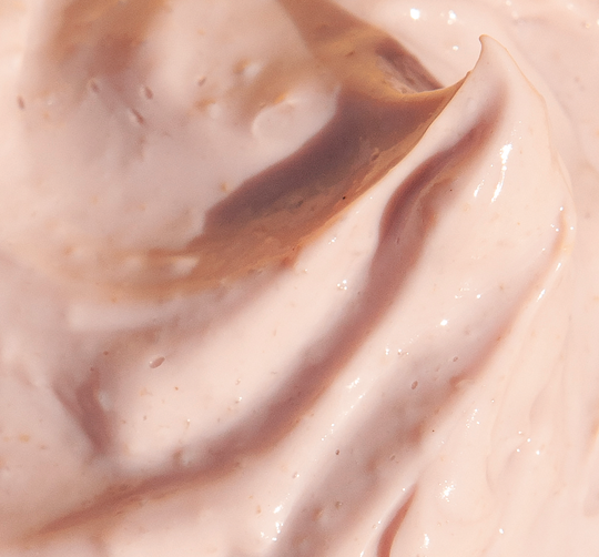 Close-up of smooth, creamy light peach skincare mask texture with small exfoliating particles, representing Mighty Brighty™ Vitamin C + Chamomile Brightening Mask | Farmhouse Fresh.
