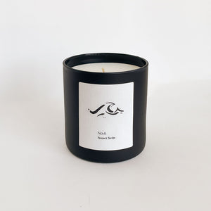 Minimalist black candle container with a white label featuring a wave design and text, showcasing No. 4 Sunset Swim (Amalfi Coast) Candle | Lucky Owl for a calming wellness ambiance.