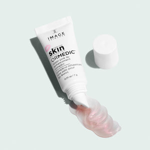The open tube of ORMEDIC sheer pink lip enhancement complex | IMAGE Skincare with a small amount of the glossy, pink tinted lip product oozing out on a light surface.