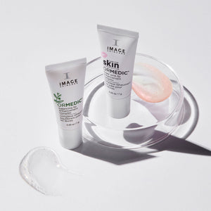 Two tubes of ORMEDIC sheer pink lip enhancement complex | IMAGE Skincare displayed with clear gel and pink balm swatches on a white surface, promoting skincare and wellness.