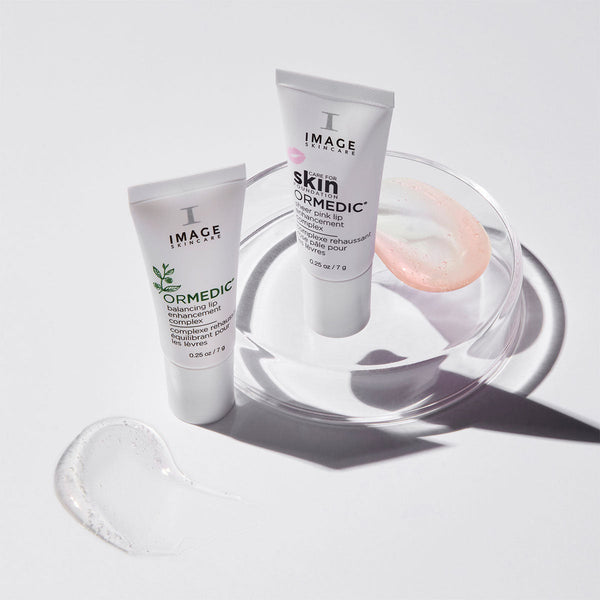 Two tubes of ORMEDIC sheer pink lip enhancement complex | IMAGE Skincare displayed with clear gel and pink balm swatches on a white surface, promoting skincare and wellness.