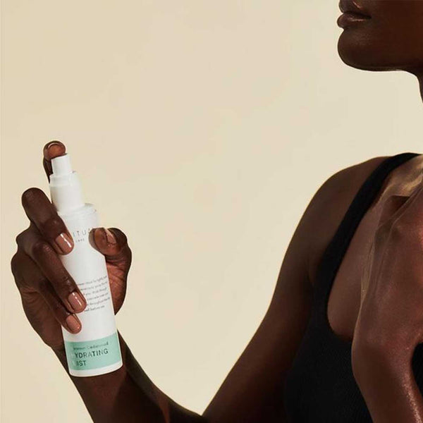Person with dark skin holding a white bottle of Geranium Cedarwood HYDRATING MIST | Sparitual, a skincare product designed for hydration and wellness.