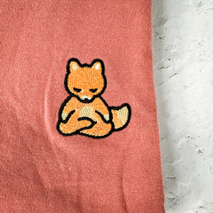 Close-up of a soft pink fabric featuring an embroidered meditating fox patch on the Meditating Fox Comfy Tee | Lucky Owl.