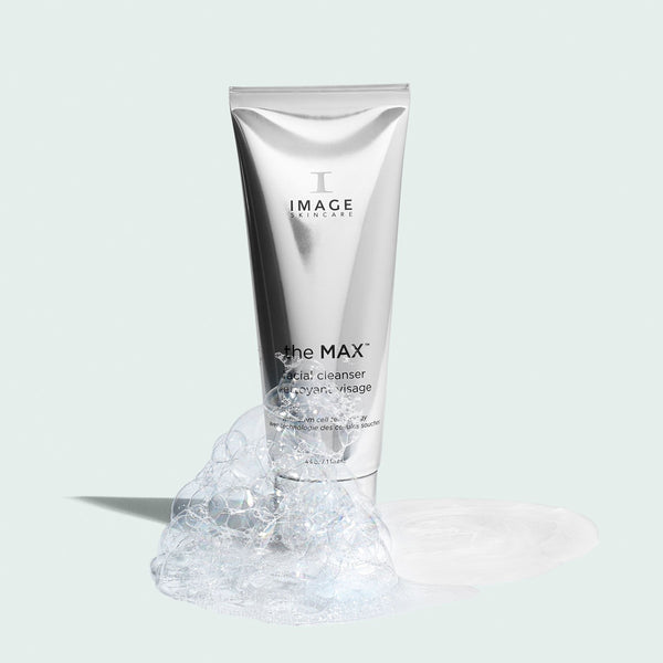 the MAX™ facial cleanser | IMAGE Skincare in a sleek silver tube surrounded by cleansing foam and bubbles on a light background, highlighting skincare and cleansing essentials