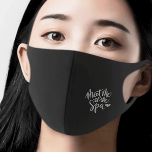 Woman wearing a black face mask printed with the phrase Meet Me at the Spa Face Mask | Lucky Owl in a calming, minimalist style promoting skincare wellness.