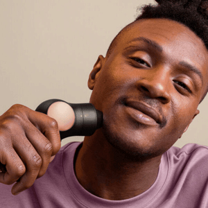 Man using a TheraFace PRO | Therabody handheld recovery tool on his neck, demonstrating skincare and wellness device for muscle relief and self-care.