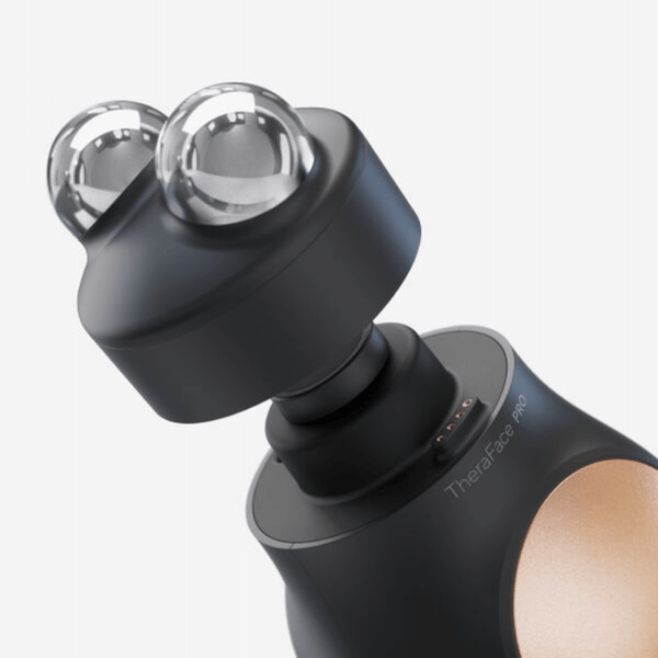 Close-up view of the black and gold TheraFace PRO | Therabody facial cleansing and recovery device with dual metallic spheres for skincare and wellness care.