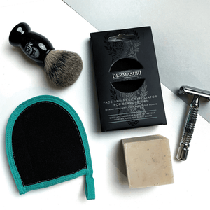 Face and Neck Scrub For Bearded Men | Dermasuri displayed with a shaving brush, razor, exfoliating soap bar, and a teal and black exfoliation mitt, highlighting men's skincare essentials.