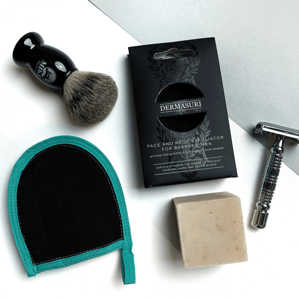 Face and Neck Scrub For Bearded Men | Dermasuri displayed with a shaving brush, razor, exfoliating soap bar, and a teal and black exfoliation mitt, highlighting men's skincare essentials.
